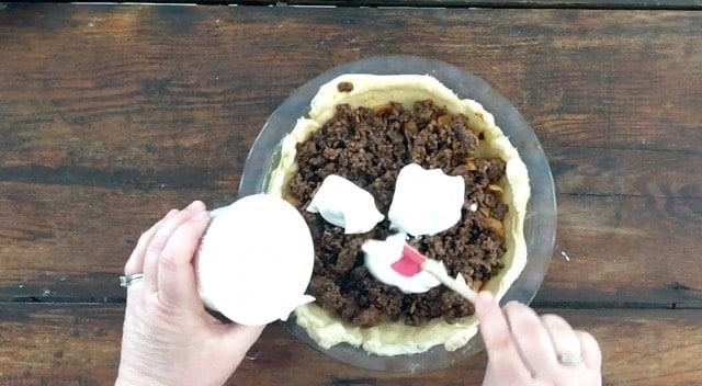 Red spatula adding dollops of sour cream to the top of the taco pie