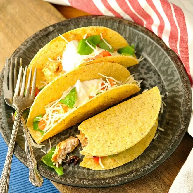 Three chicken tacos on a grey plate with a red and white napkin
