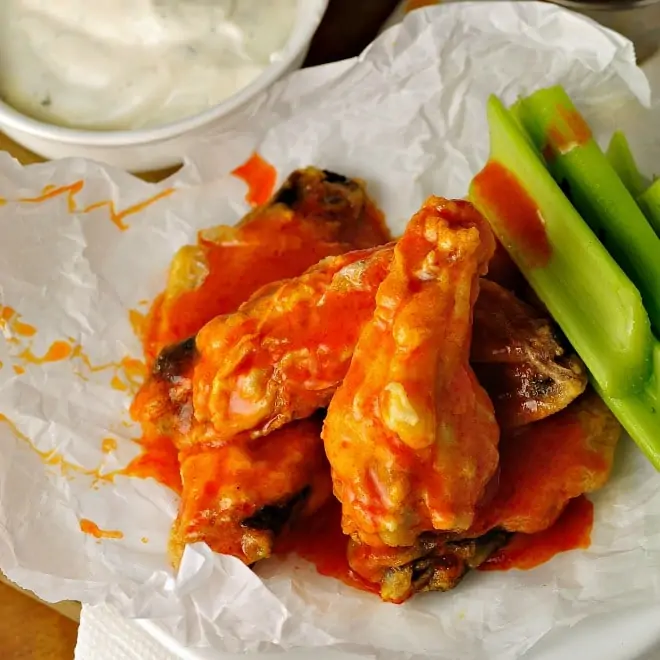 Healthier Baked Chicken Wings on wax paper with buffalo sauce