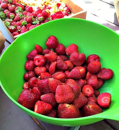 a green bowl of fresh strawberries with a box of them in the background