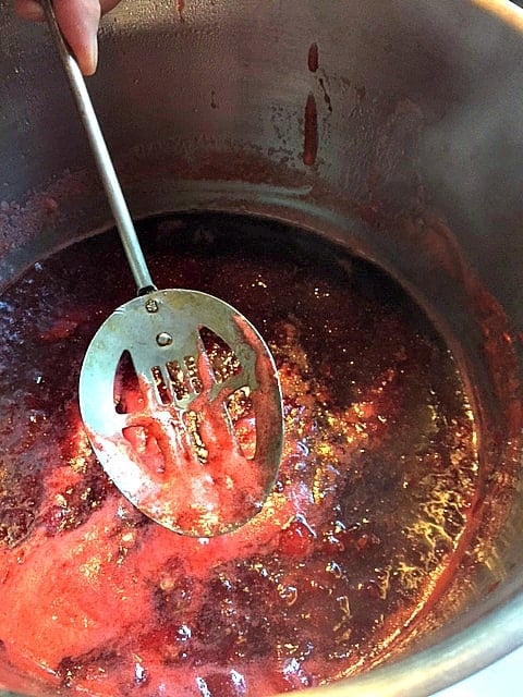 slotted spoon skimming foam off of the top of strawberry jam