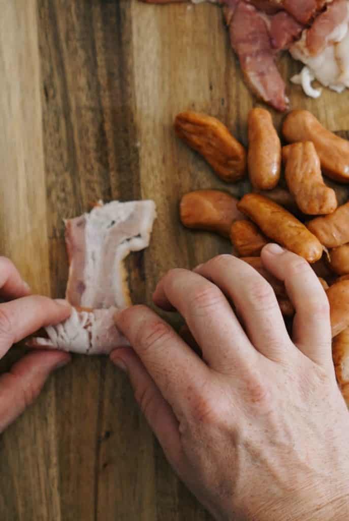 A photo of wrapping the bacon around the smoky for candied bacon wrapped smokies