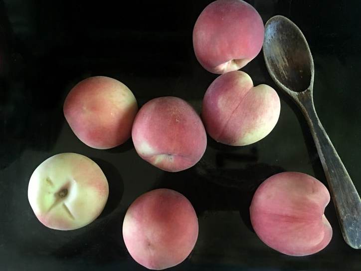 whole fresh peaches with wooden spoon