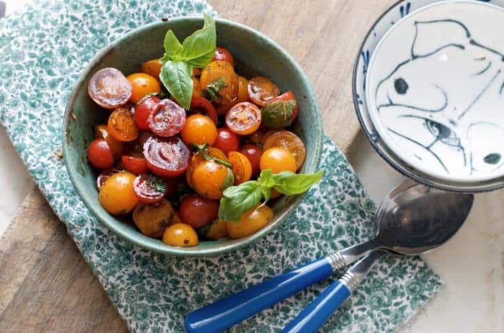 A photo from above of Summer Cherry Tomato Salad showing some blue silverware and smaller serving dishes