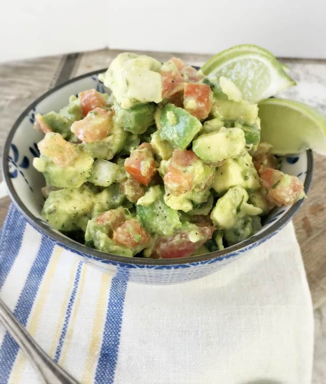 Side view of guacamole dip with limes in blue bowl and napkin