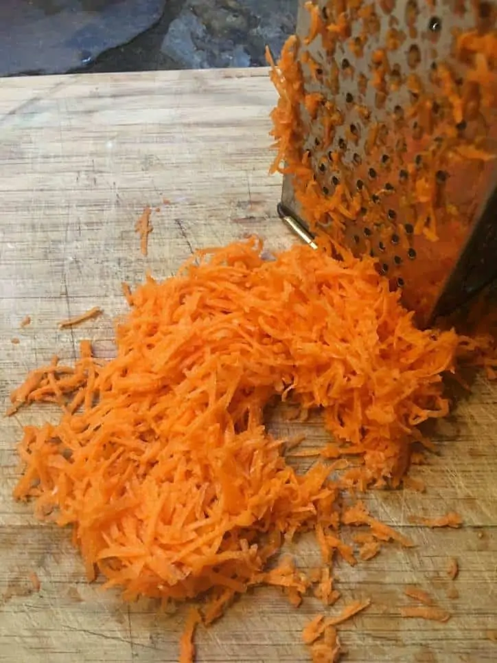 a photo of grated carrots, cutting board and box grater