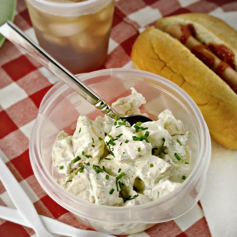 Bowl of potato salad with hot dog and iced tea in the background