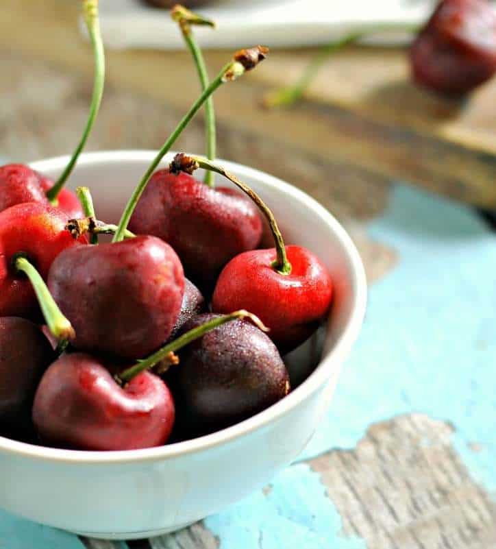 A bowl of tart cherries in a white bowl on a blue chipped wood background