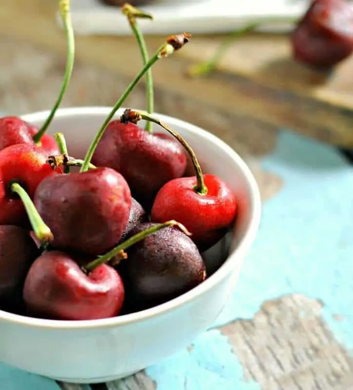 A bowl of tart cherries in a white bowl on a blue chipped wood background