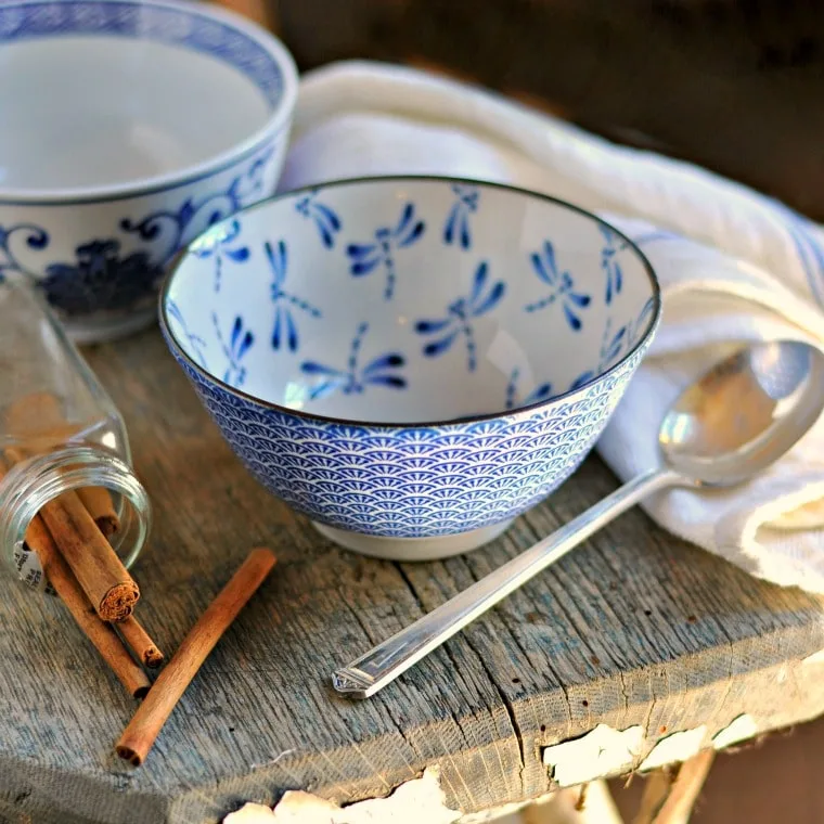 An empty blue bowl with a dragon fly print, cinnamon sticks, a spoon and a kitchen towel