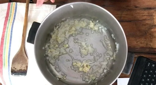 A large stock pot with onion and garlic sauteing in the bottom of the pot