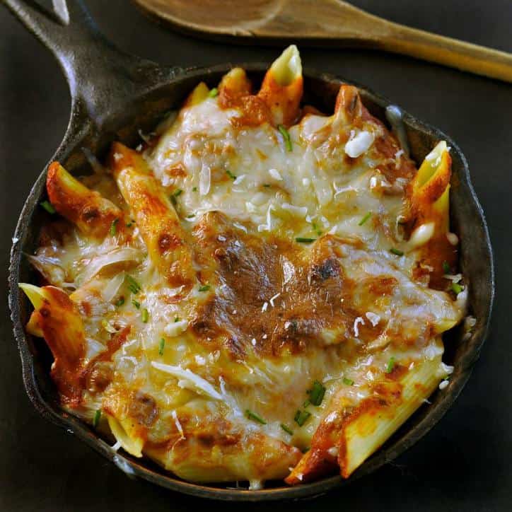 Black Cast iron skillet and wooden spoon with cheese and sauce covered pasta in the skillet.