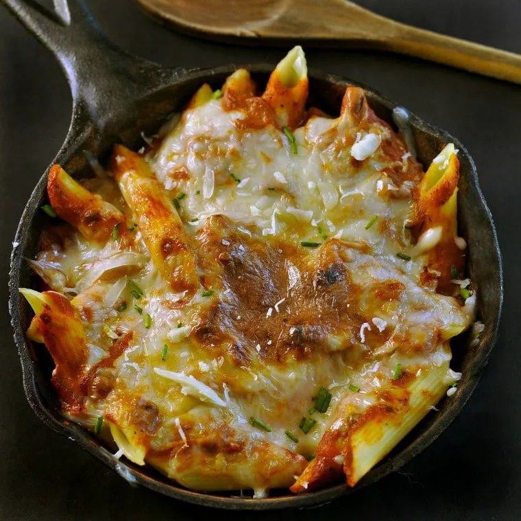 Black Cast iron skillet and wooden spoon with cheese and sauce covered pasta in the skillet.