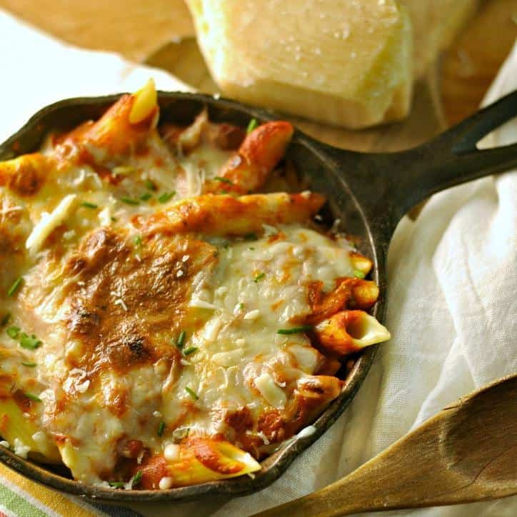 The sunlight glistening off of a cast iron skillet filled with pasta and sauce sitting on a white linen napkin with wooden spoon