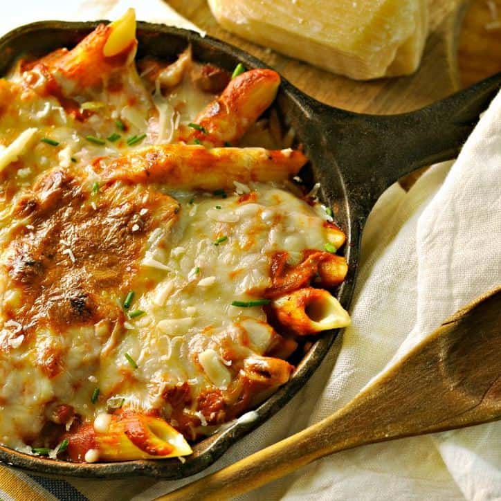 wooden spoon, white linen napkin and cast iron skillet filled with pasta covered with san marzano tomato sauce and melted cheese