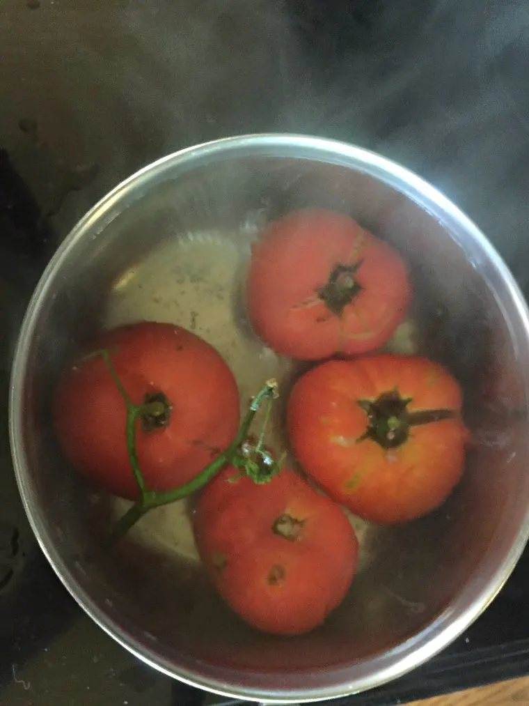 four tomatoes in a pan of boiling water