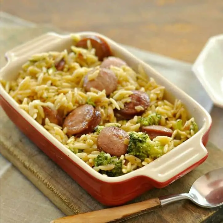 A casserole dish and a spoon of Smoked Sausage and Cheesy Orzo @loavesanddishes.net