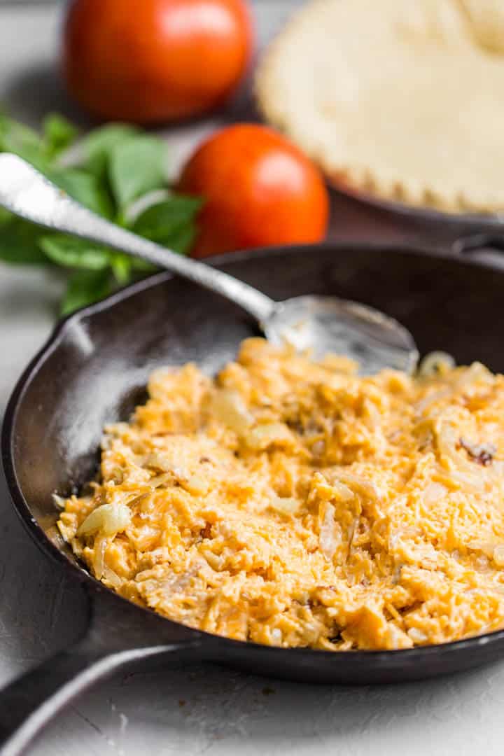 cheese mixture in a cast iron skillet with tomatoes and basil in background