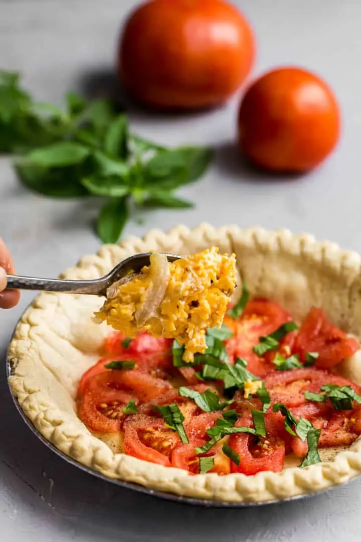 parbaked pie shell with layer of tomatoes, herbs and cheese mix being spooned on.