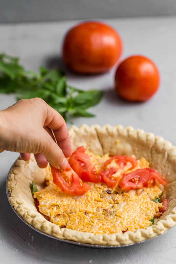 Tomatoes being laid in pie dish for tomato pie