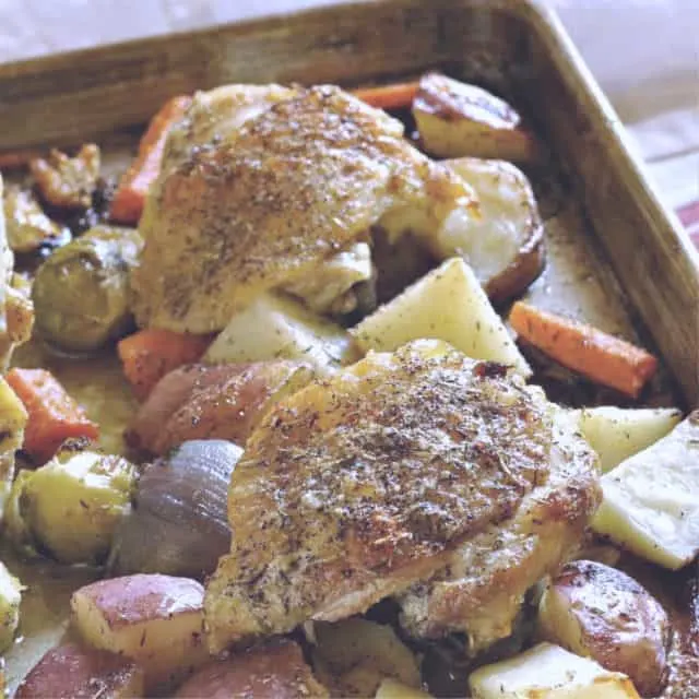 Two Chicken thighs with crispy skin on a sheet pan with veggies