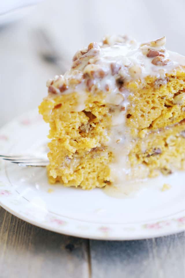 A side view of a slice of pumpkin praline cake showing the tender and moist center with icing running down the side of the cake