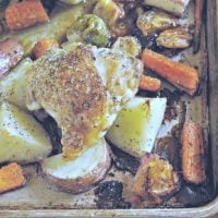 Photo showing crispy Chicken thigh on a sheet pan of potatoes and carrots