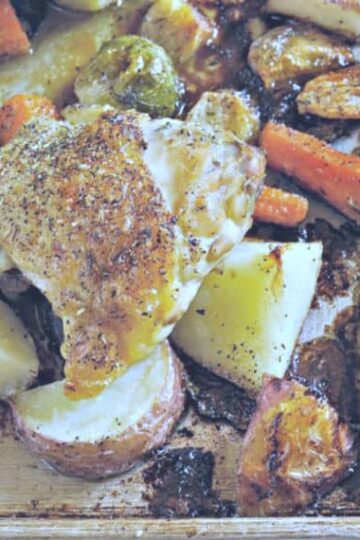 Photo showing crispy Chicken thigh on a sheet pan of potatoes and carrots