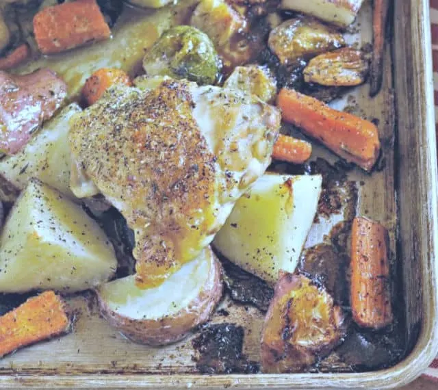 Photo showing crispy Chicken thigh on a sheet pan of potatoes and carrots