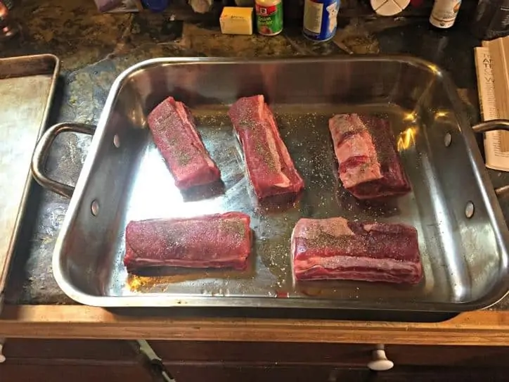 Ribs in a silver baking dish with salt and pepper