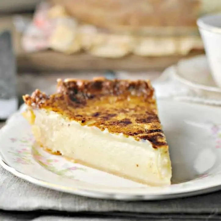 a photo of a slice of sugar cream pie from the left on a china plate on a tan linen napkin