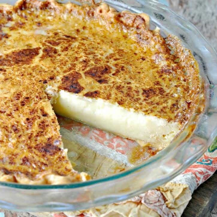 A photo of a slice out of a whole old fashioned sugar cream pie in a glass pie plate on a kitchen towel