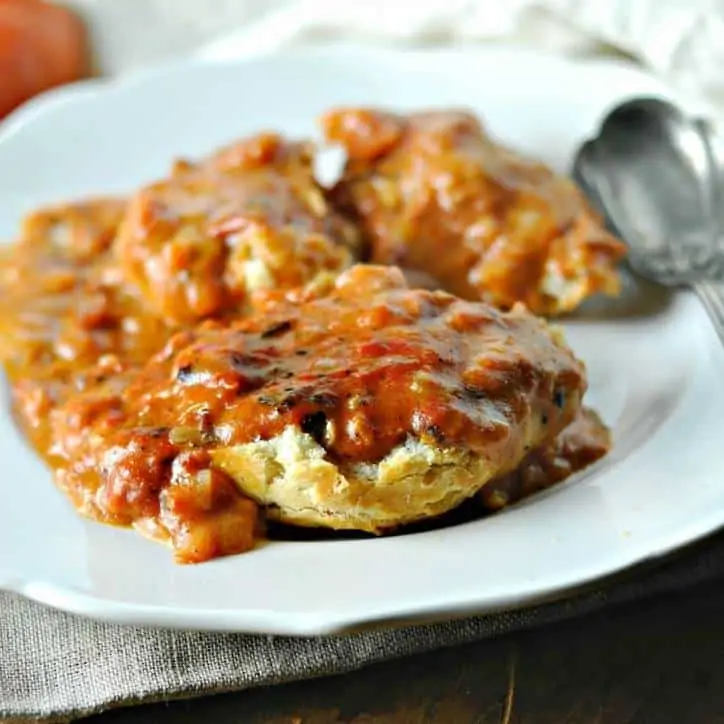a white plate and a spoon with a biscuit covered in tomato gravy