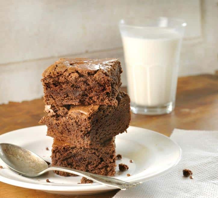 Stack of three of the best brownies in the world on white plate with spoon and glass of milk
