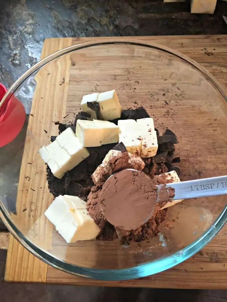 glass bowl on cutting board with chocolate and butter and cocoa in bowl