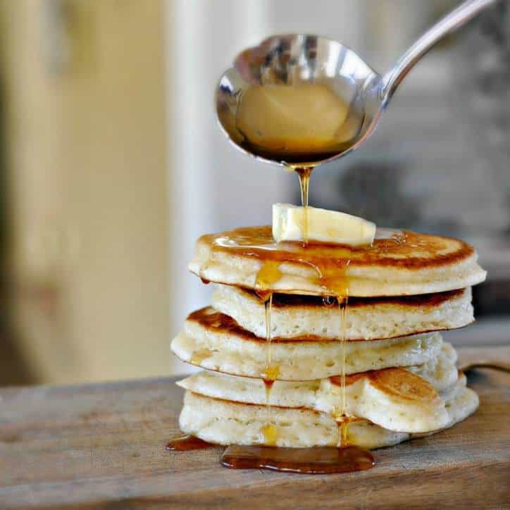 stack of four pancakes on a wooden board with butter pat and syrup dripping down