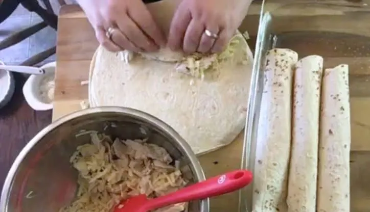 hands rolling up flour tortillas with chicken