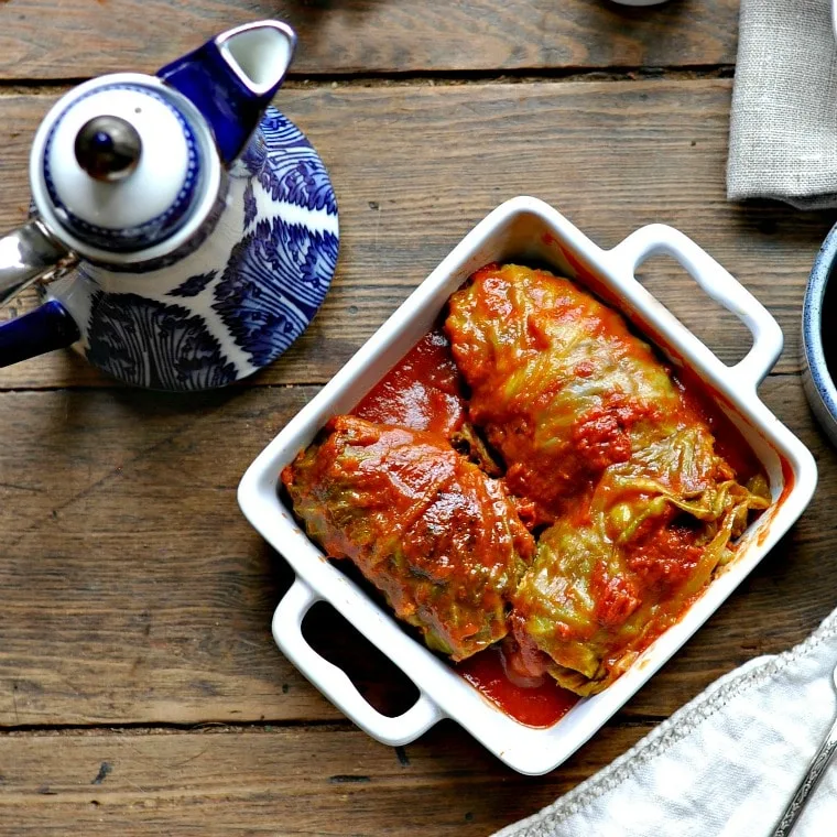Square white dish holding three classic cabbage rolls with russian tea pot in background