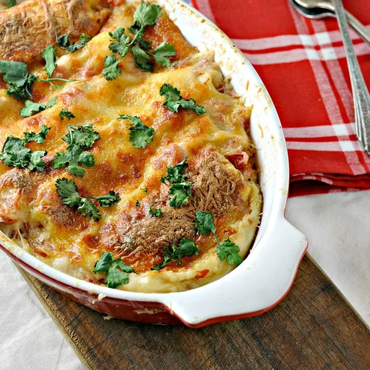 Red baking dish with easy cheesy white chicken enchiladas and a red napkin