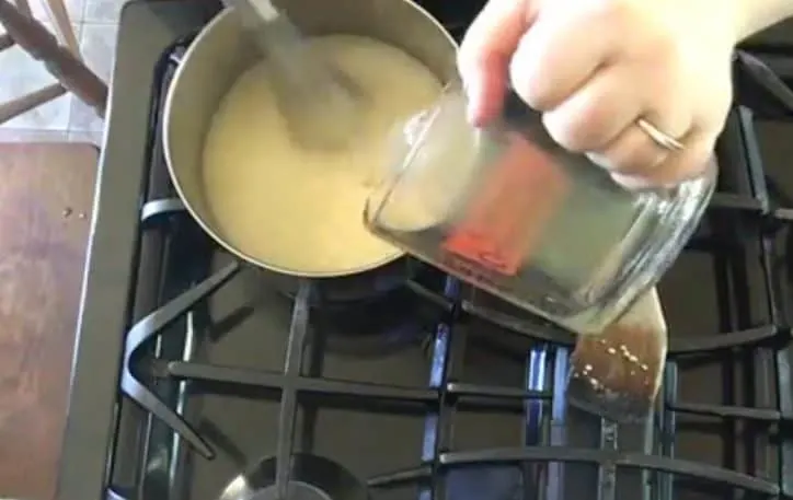 pouring stock into cheesy sauce on stove top