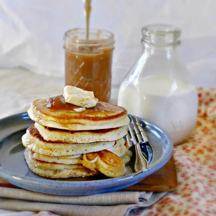 Stack of pancakes on a blue plate with fork, apple butter and milk in the background