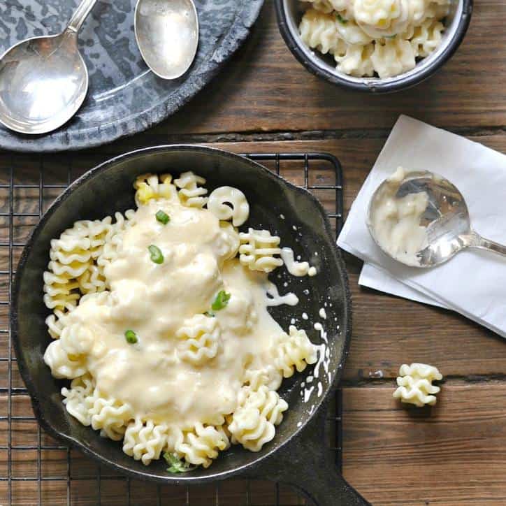 Small black bowl of mac and cheese on wooden table with spoons