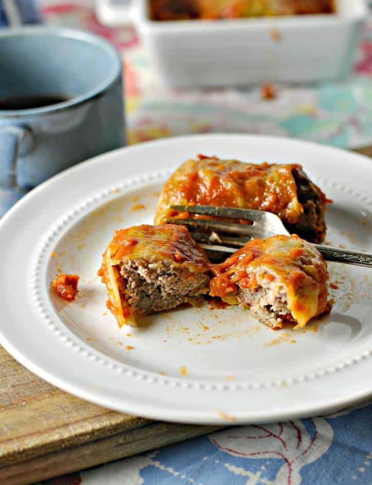 a small white plate with one cabbage roll cut in two and a whole one in back. 