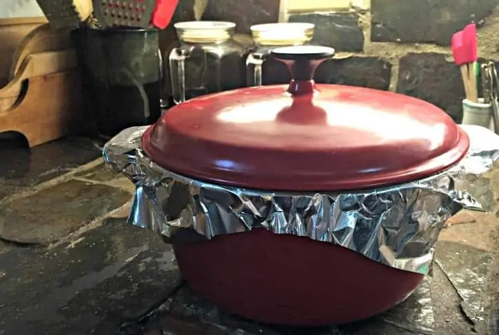 red dutch oven with aluminum foil over the top and the lid on top of that.