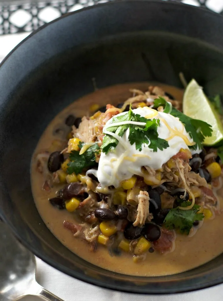 Black bowl filled with chicken chili topped with sour cream.