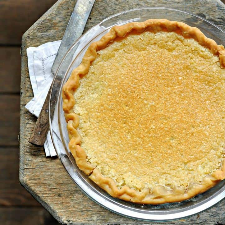 A view of a whole vinegar pie in a glass pie plate, white napkin, old knife shot from above