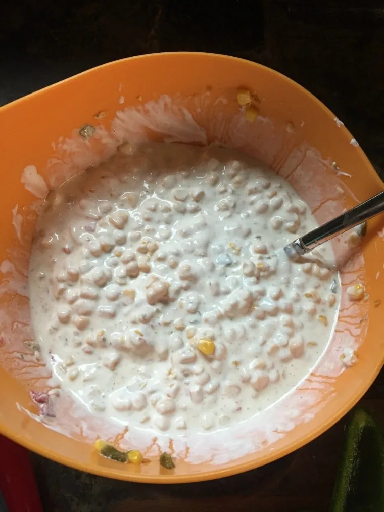 Large orange bowl with corn dip ingredients mixed together and spoon