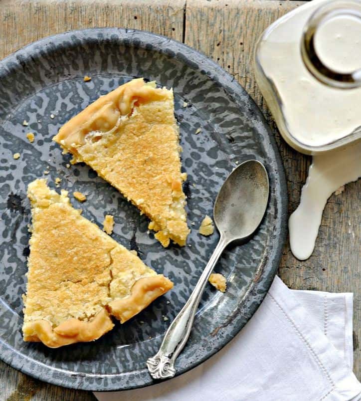 A shot from above a grey speckled plate with two slices of pie, spoon, spilled milk bottle and white napkin