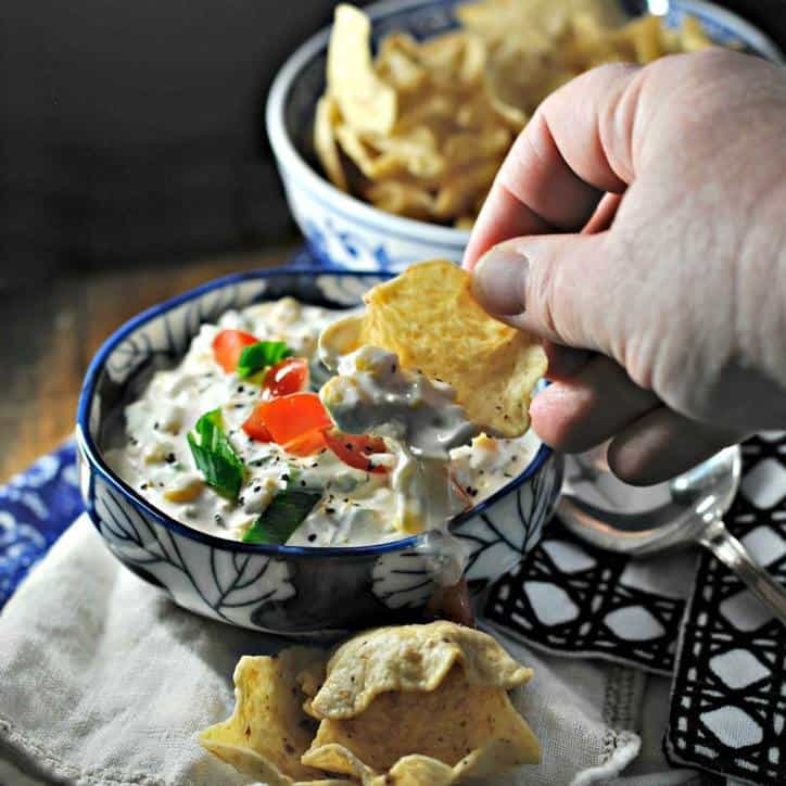 Hand scooping corn dip with chip. Blue bowl and napkin in background