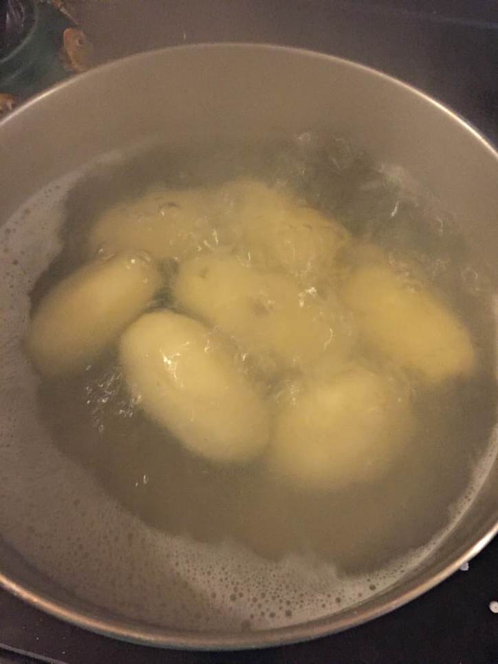 a large pot of boiling whole white potatoes with steam rising.